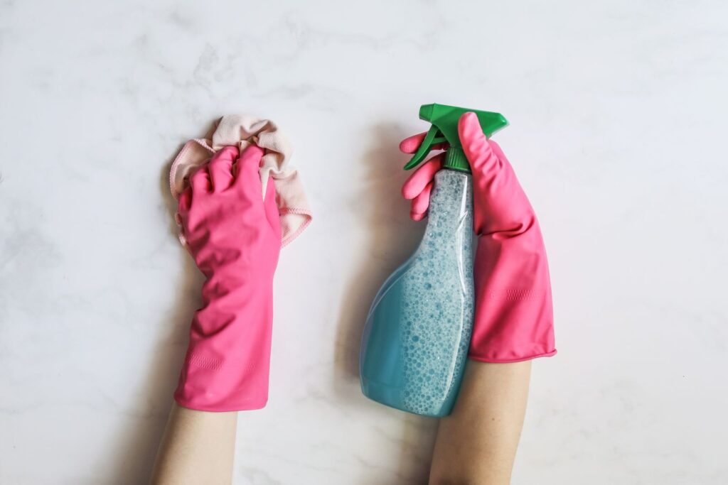 Hands in pink rubber gloves holding a cloth and a spray bottle